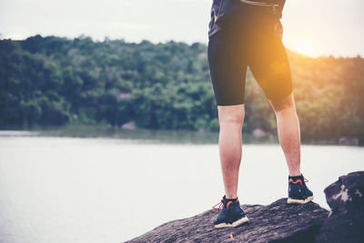 Low section of man standing on rock against lake