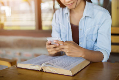 Midsection of woman reading book while sitting on table