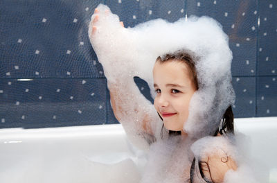 Smiling girl playing with soap sud in bathtub