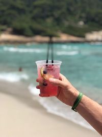 Cropped hand holding drink at beach