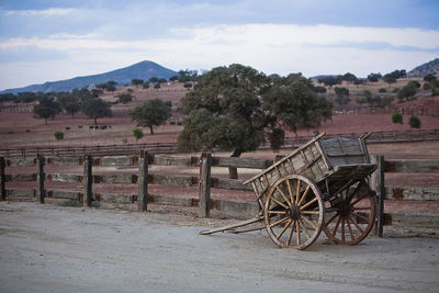 Abandoned cart on field by trees against sky