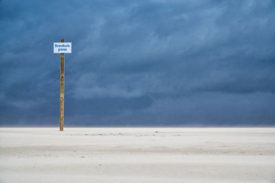 Sign board on beach against sky