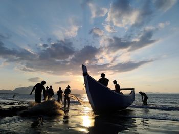 Silhouette people on beach against sky during sunset