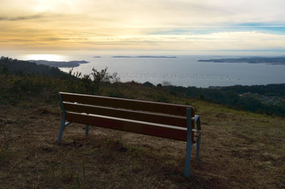 Empty bench on lakeshore against cloudy sky