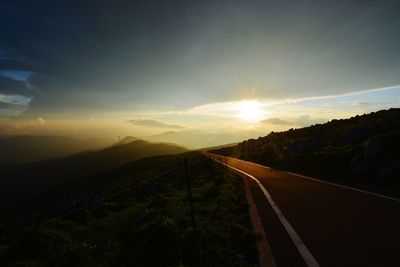 Road by mountains against sky during sunset