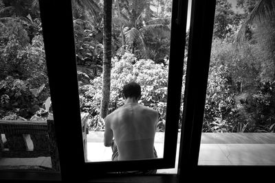 Rear view of shirtless man looking through window