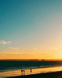 People riding bicycle on beach against sky during sunset