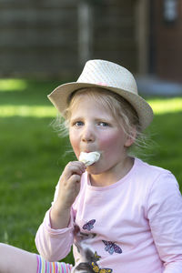 Portrait of cute girl eating ice cream while siting on field at park