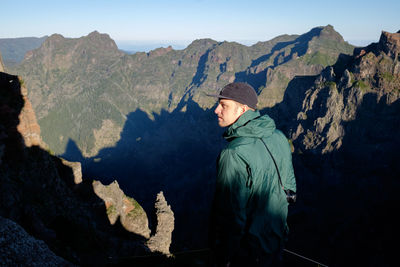 Man standing on rock by mountains against sky