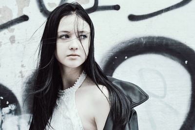 Close-up of beautiful woman looking away while standing by graffiti wall