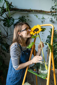 Young woman with pink flower standing against plants