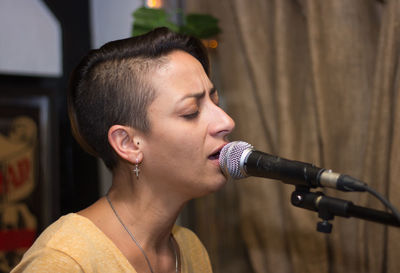 Close-up of woman with eyes closed and short hair singing in microphone