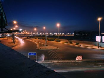 Road by illuminated city against sky at night