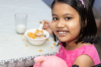 An indian girl child eating cereal and milk with smiling face and looking at camera