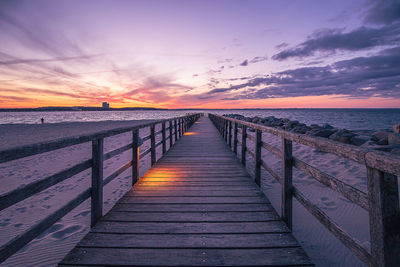 Wooden bridge over sea against sky during sunset