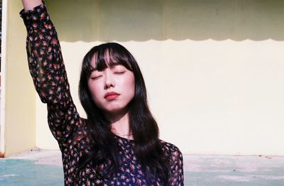 Beautiful young woman with eyes closed standing against wall