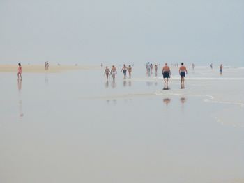 People walking at beach against clear sky