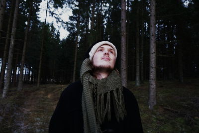 Thoughtful man standing against trees at forest