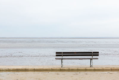 Empty bench on beach against sky