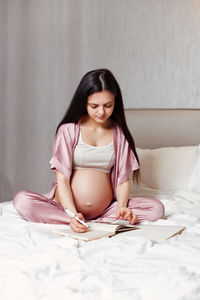 Pregnant woman writing on bed at home