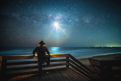 Rear view of woman standing against sea against sky at night