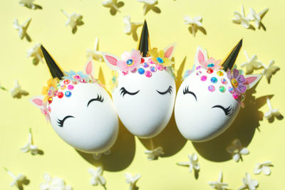 Three easter eggs in the form of a unicorn with white delicate flowers around on a yellow background