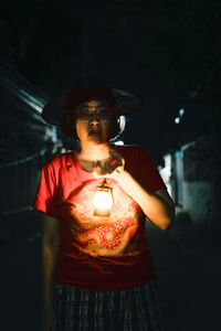 Woman wearing hat standing against illuminated lamp at night