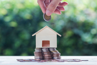 Close-up of hand holding coin over model home on table