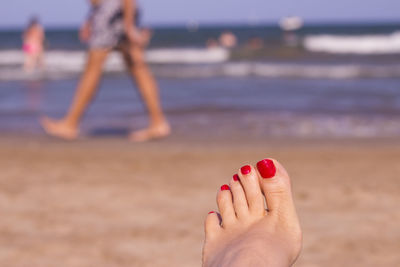 Low section of woman with red nail polish at beach