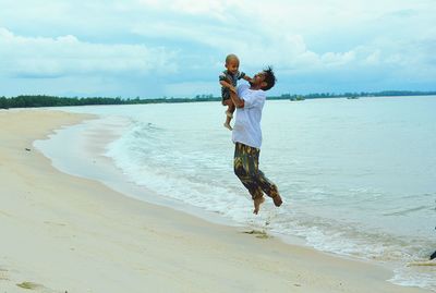 Full length of father and son at beach against sky