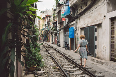 Rear view full length of woman walking amidst buildings on railroad track