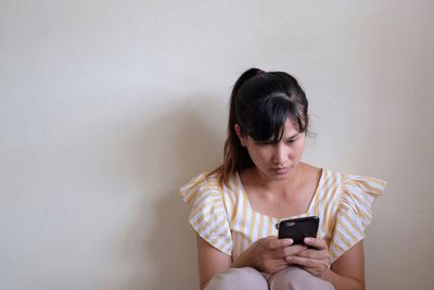 Young woman using mobile phone against wall