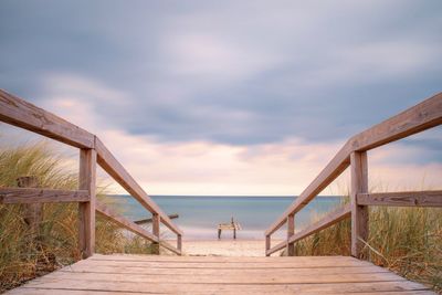 Wooden railing on beach against sky