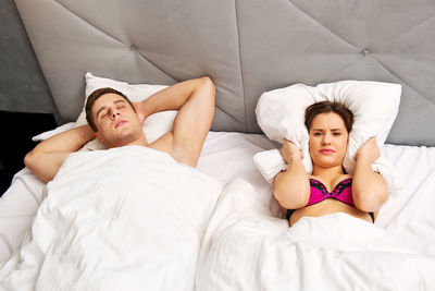 High angle view of woman covering ears with pillow while man snoring in bed at home