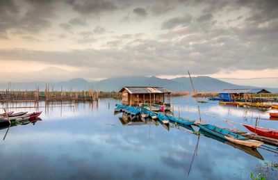 Sailboats moored in lake against cloudy sky