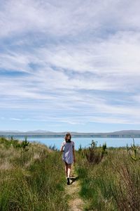 Full length of girl walking towards lake against sky