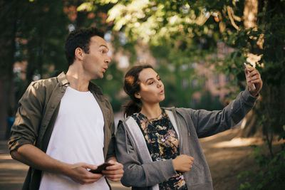 Cheerful woman taking selfie with male friend from smart phone