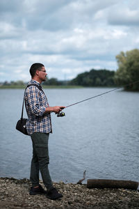 Full length of man fishing on lake against sky