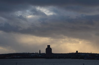 Sea by buildings against sky at sunset