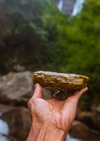 Human hand holding rock against river water and stones