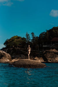 A young woman with golden skin stands in the middle of the ocean