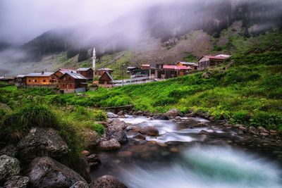 Stream amidst houses and trees against mountains