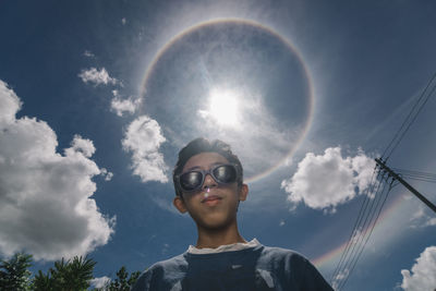 Low angle portrait of boy wearing sunglasses standing against sky during sunny day