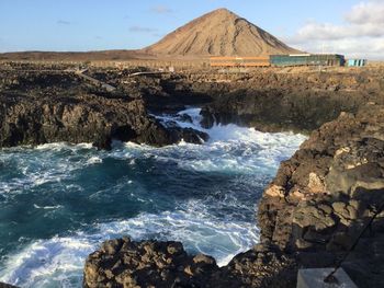 Scenic view of rocky shore by sea against sky