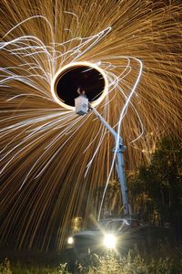 Low angle view of man spinning wire wool on cherry picker at night
