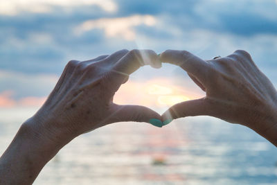 Cropped image of hand holding heart shape against sky