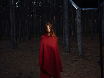 Portrait of woman standing by tree trunk in forest