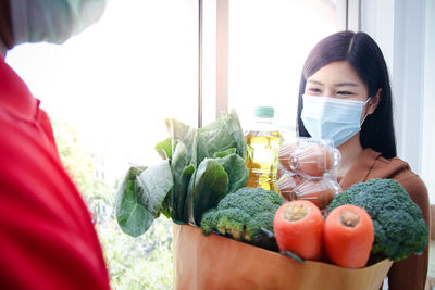 Smiling woman wearing mask taking delivery of vegetables at home