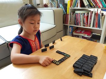 Cute girl playing with dominoes on table