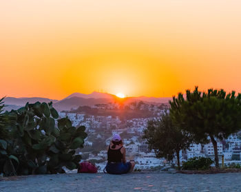 Rear view of woman sitting on beach against sky during sunset